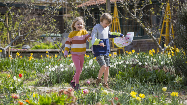 Two children on an Easter egg hunt at Osterley, walking through the Kitchen Garden